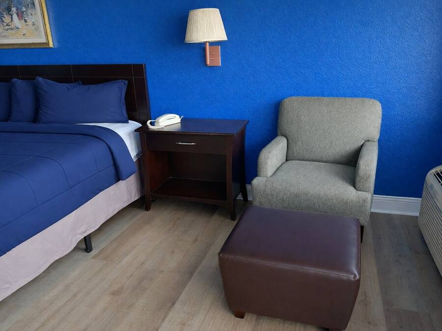 A hotel room with a bed, a nightstand, a chair, and a heater.