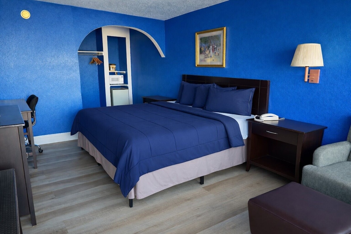 A hotel room with a large bed, a desk, a chair, a lamp, and a picture on the wall.