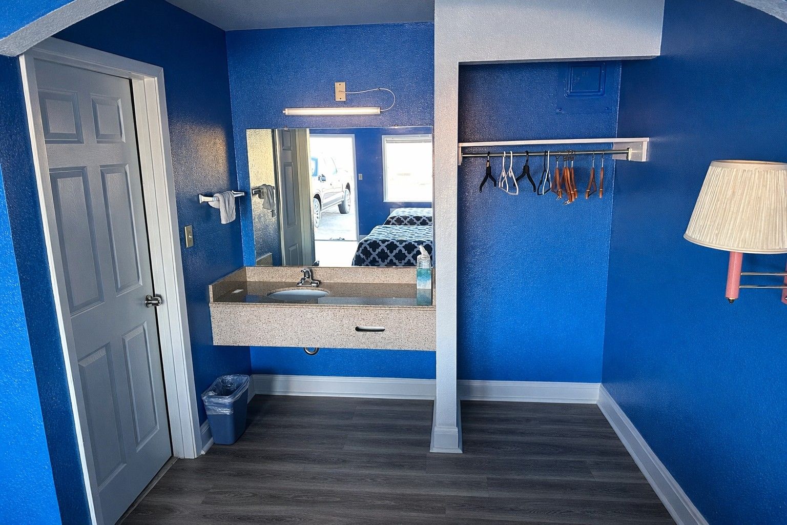 A bathroom with a blue wall, a sink, a mirror, a towel rack, and a trash bin.