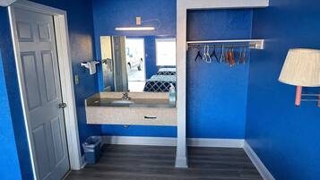 A bathroom with a blue wall, a sink, a mirror, a towel rack, and a trash bin.