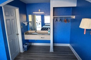 A bathroom with a blue wall, a sink, a mirror, a towel rack, and a trash bin.
