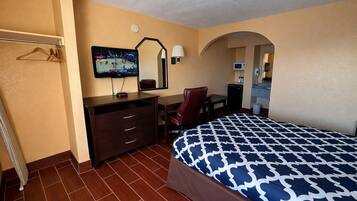 A hotel room with a bed, a desk, a chair, a TV, and a mirror.