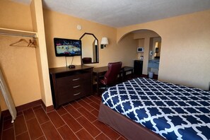 Habitació d'hotel amb llit, escriptori, cadira, televisió i mirall.
