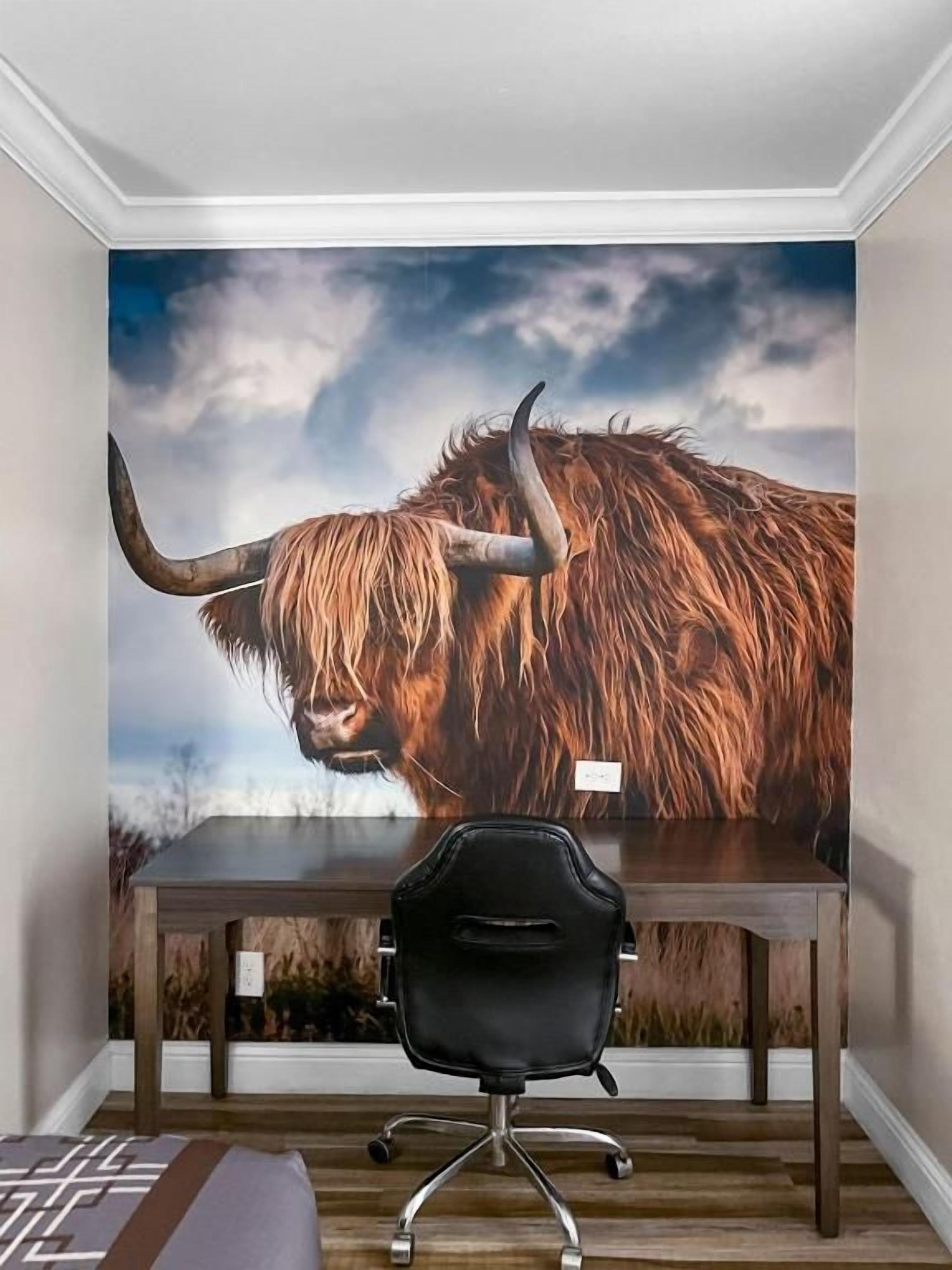 A room with a large bull mural on the wall, a wooden desk, and a black office chair.