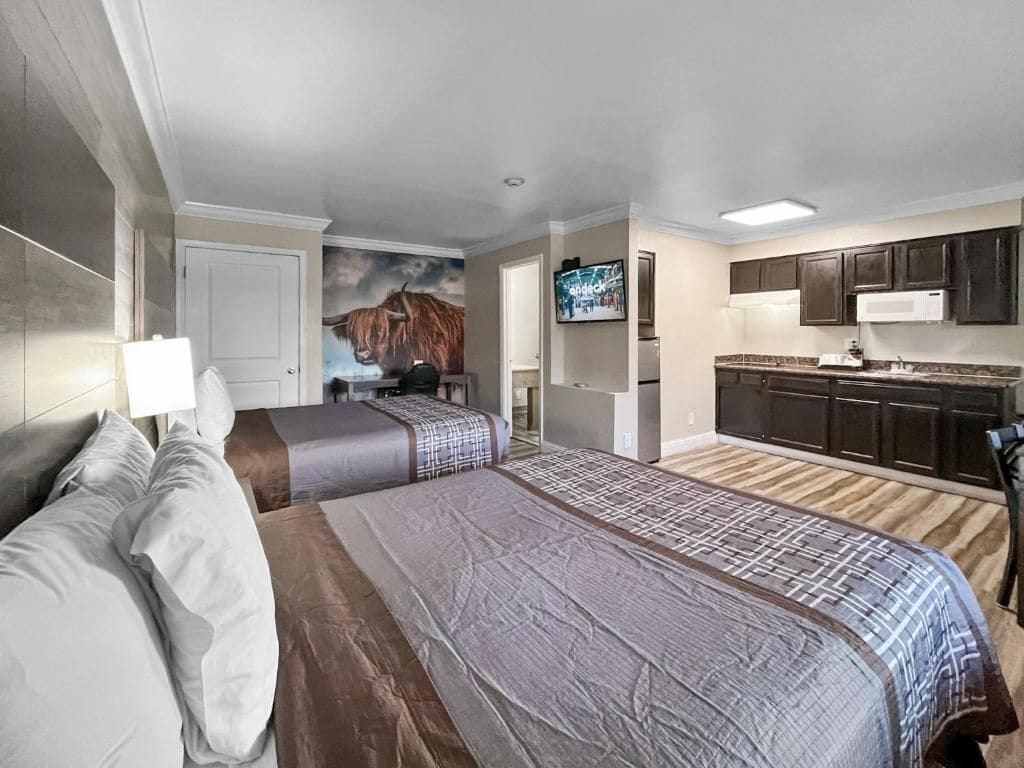A hotel room with two beds, a kitchenette, and a television.