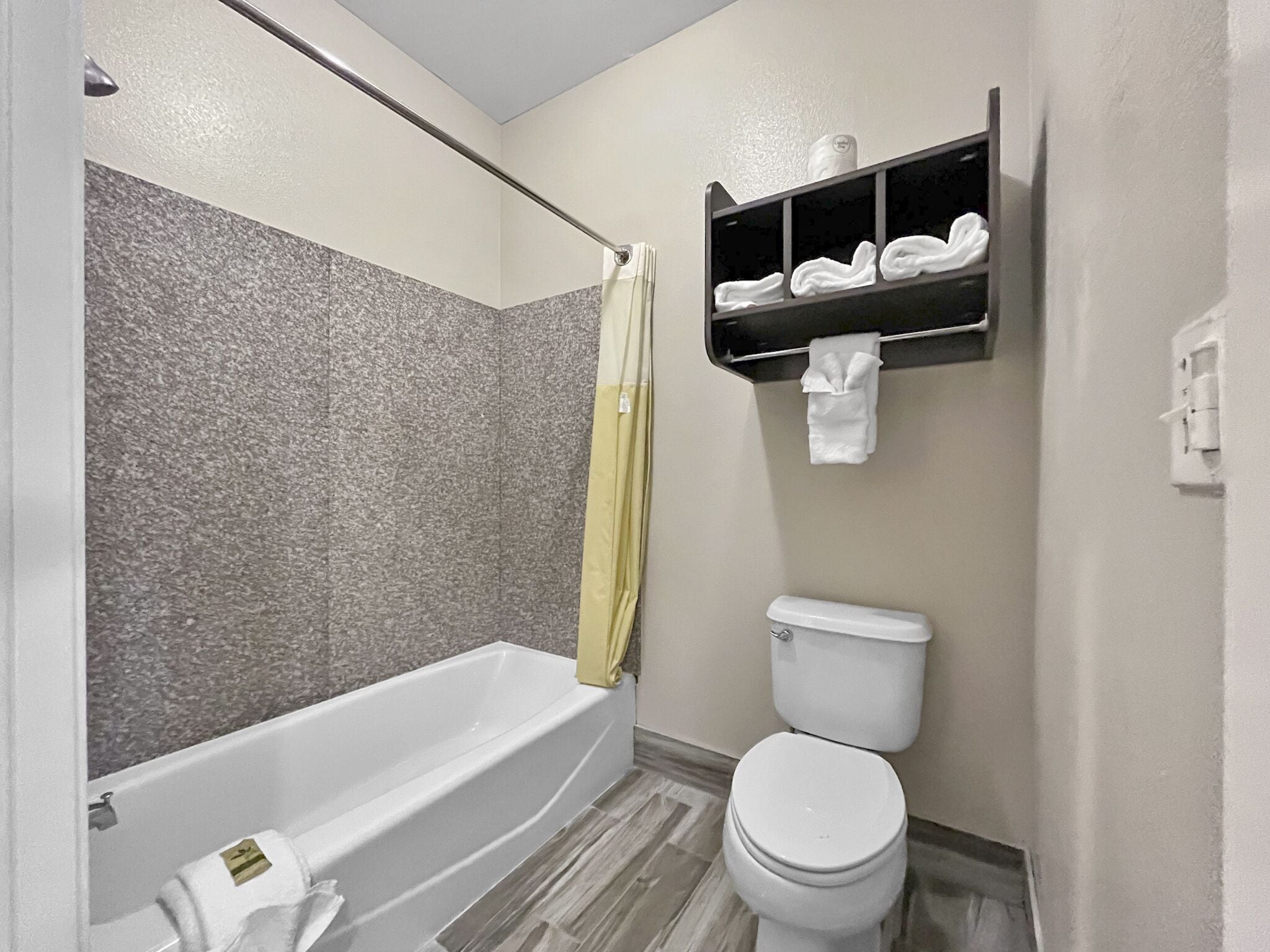 A bathroom with a bathtub, toilet, and a shelf with toiletries.