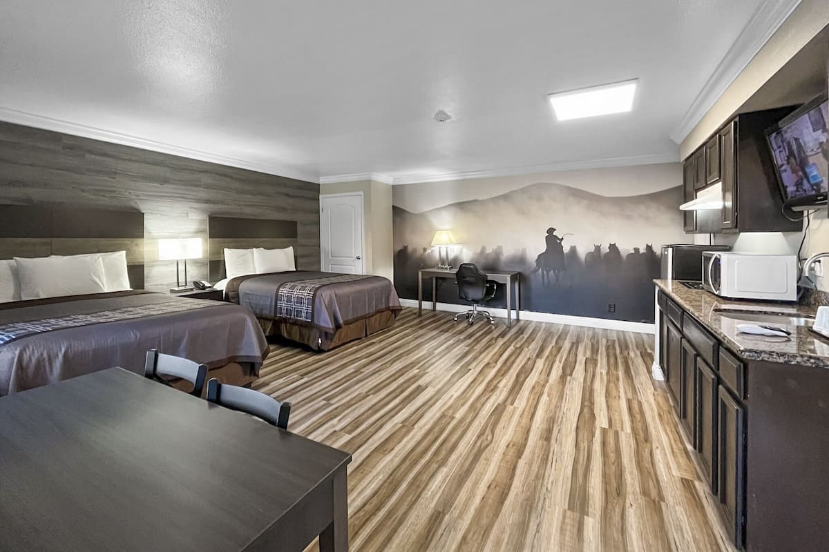 Una habitación de hotel con dos camas, un escritorio, una silla, un televisor y un microondas.