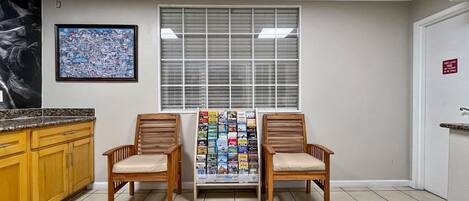 A waiting area with two wooden chairs, a bulletin board with magazines, a large window with blinds, a framed map on the wall, and a kitchen counter.