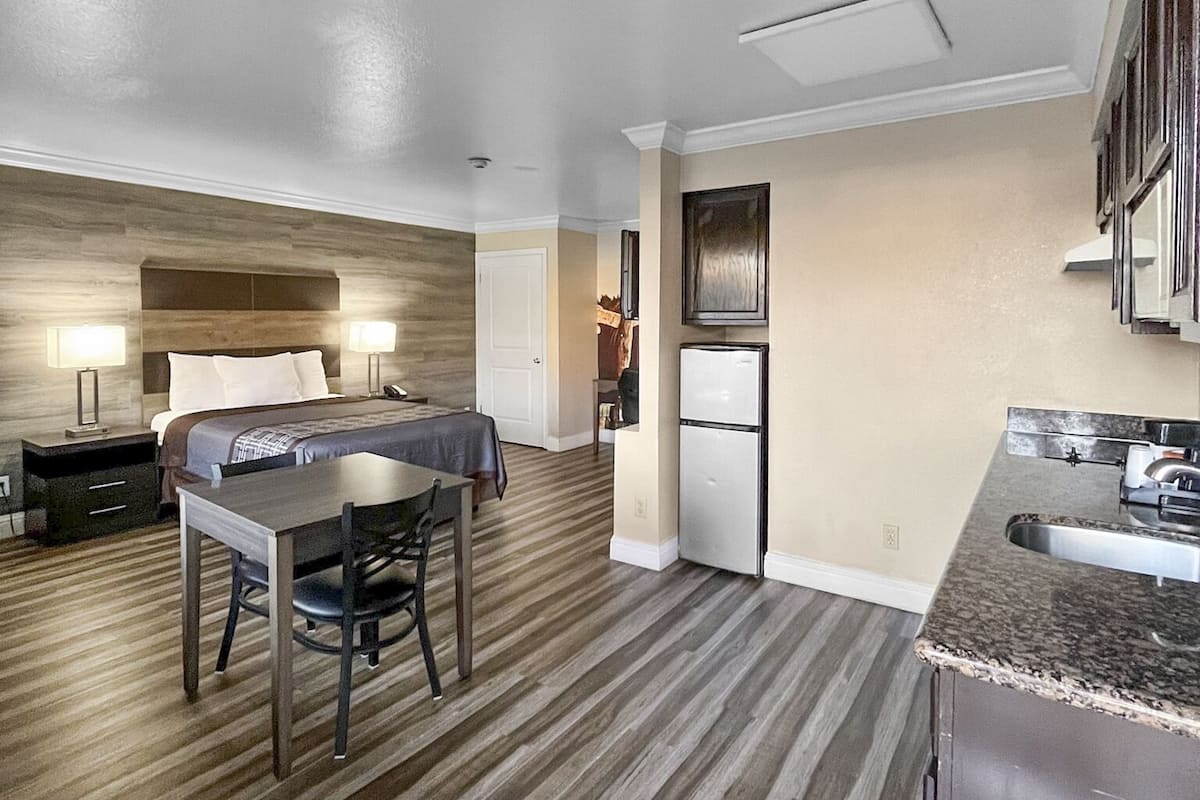 Una cocina moderna con refrigerador empotrado, un comedor con mesa y sillas, y un dormitorio con cama y mesitas de noche.