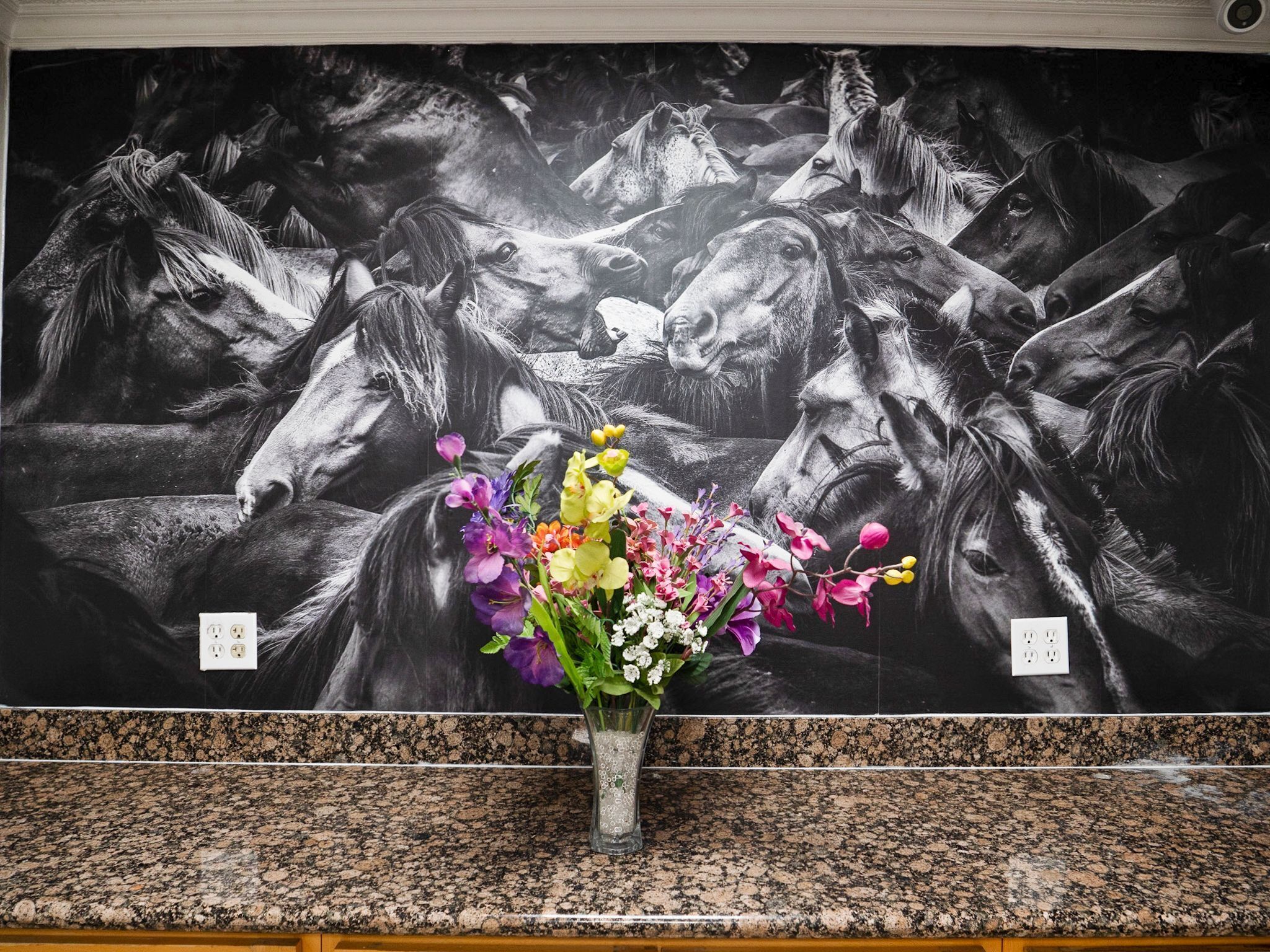 A wall mural of horses with a vase of flowers in front.