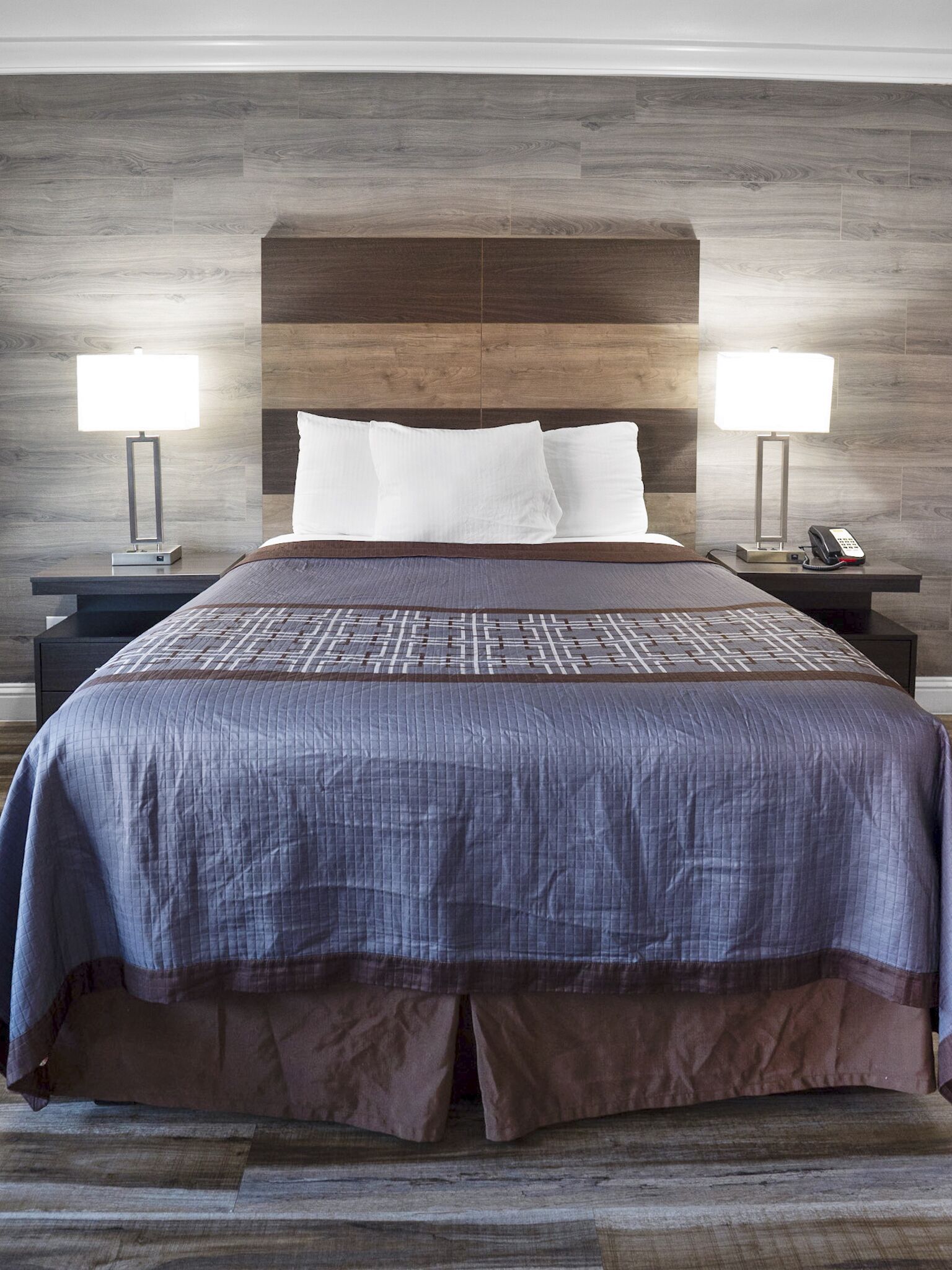 A hotel room with a large bed, two bedside tables with lamps, a telephone, and a wooden headboard.