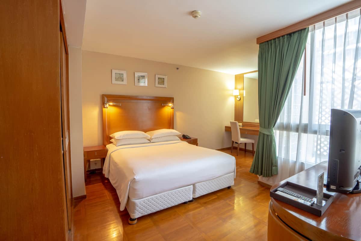 A hotel room with a large bed, a desk with a computer, a chair, and a window with curtains.