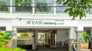 La entrada de AT EASE saladaeng by AT EATAS, con un letrero acogedor, plantas en macetas y una vista despejada del restaurante.