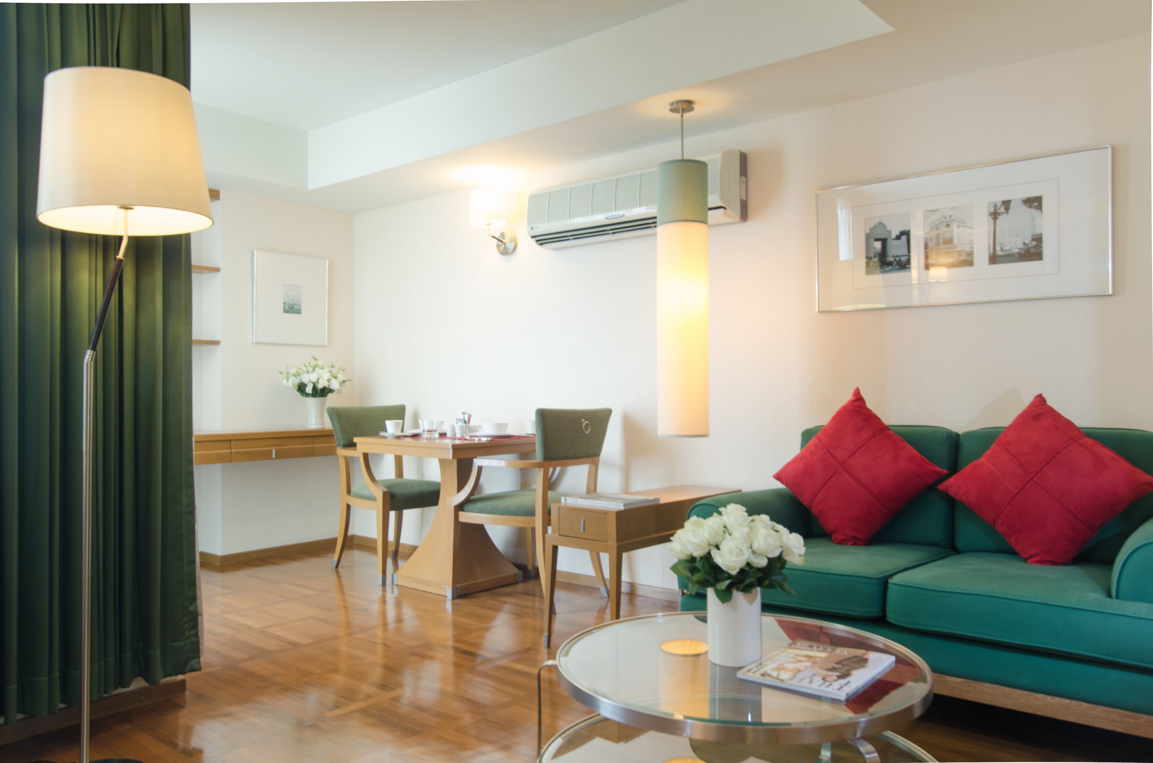 A modern living room with a green sofa, red cushions, a glass coffee table, and a dining area with wooden furniture.