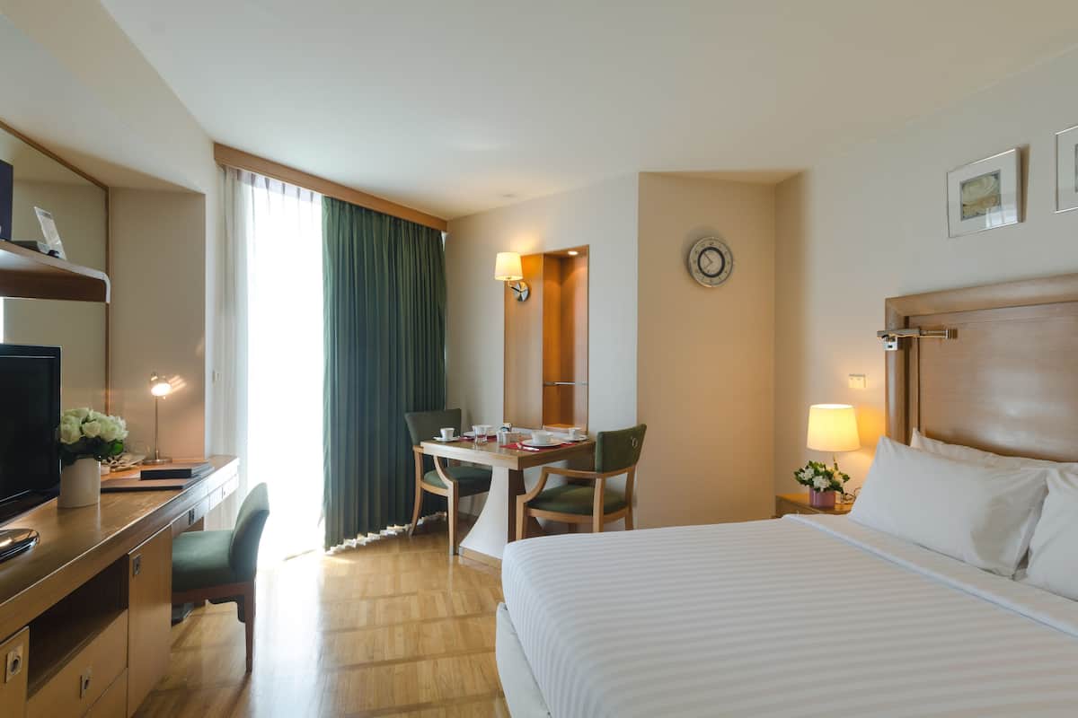 A hotel room with a bed, desk, chairs, and a television.
