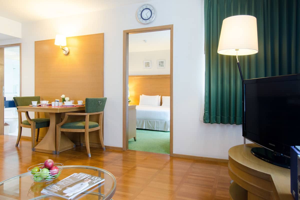 A hotel room with a dining area, a bed, a television, and a green curtain.
