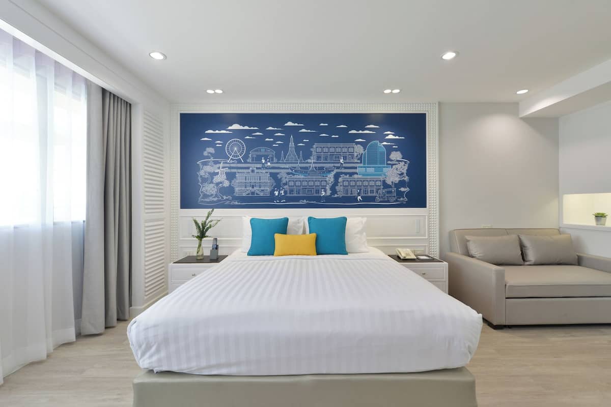 Een moderne hotelkamer met een groot bed, een slaapbank, een stadsgezicht muurschildering en een groot raam met gordijnen.