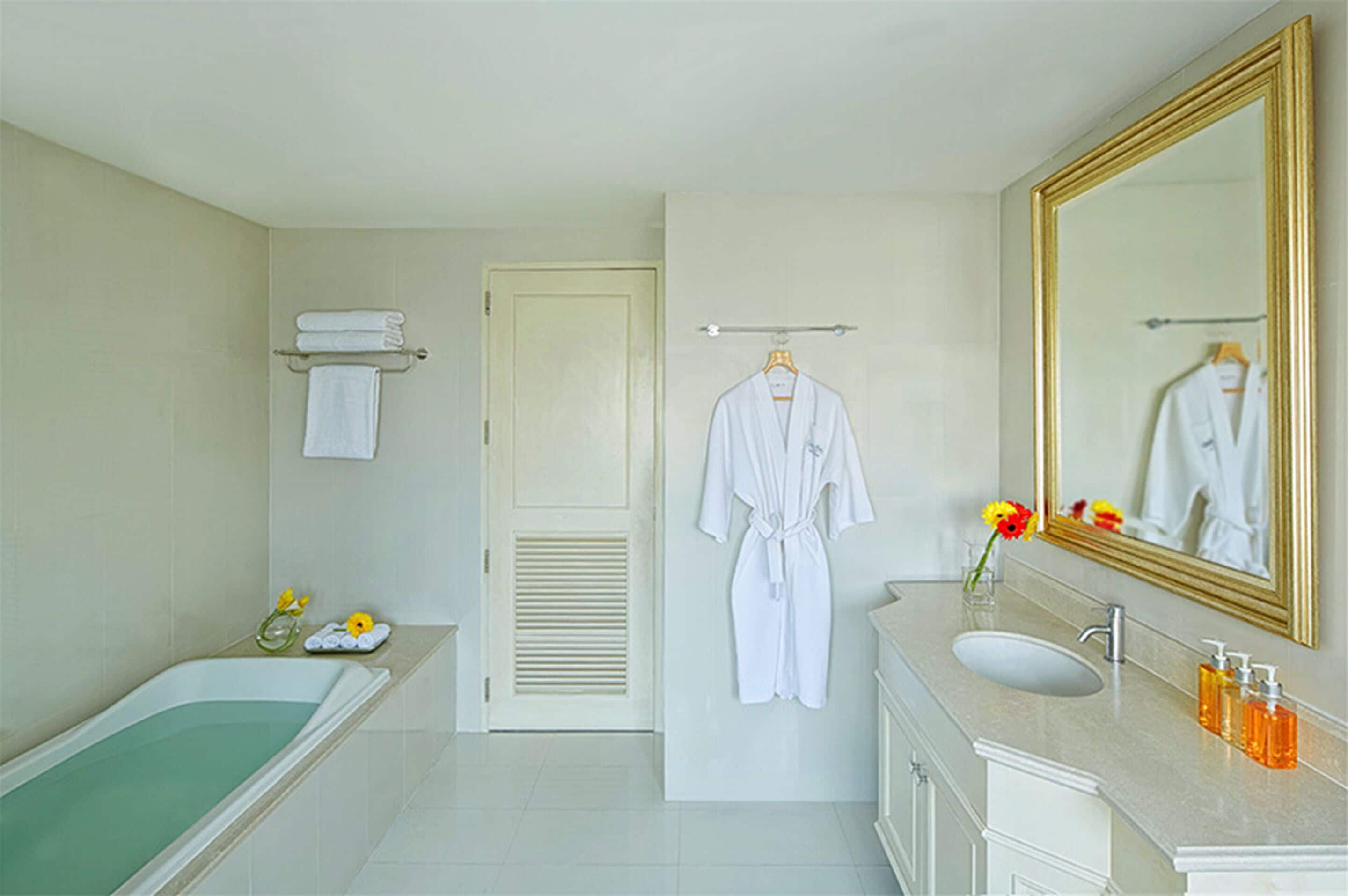 A bathroom with a bathtub, sink, and mirror. There are towels and toiletries on the counter.
