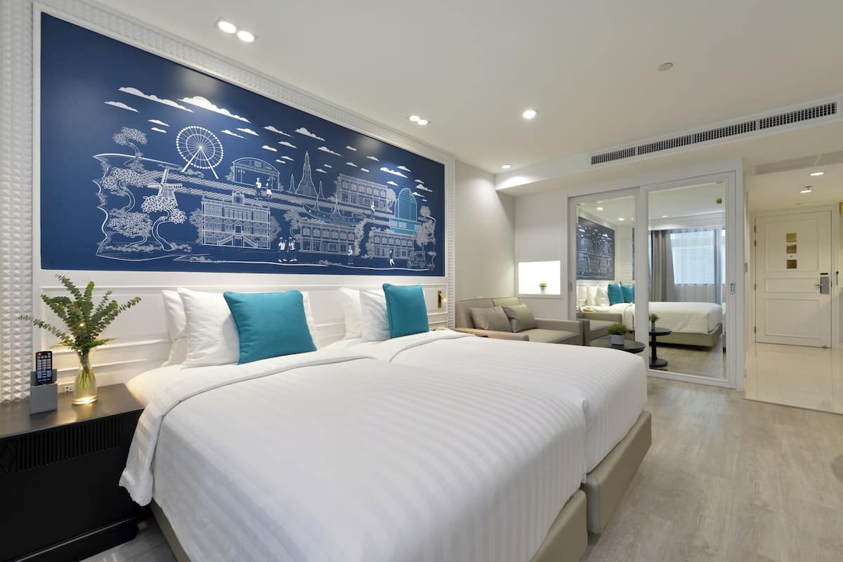 Een moderne hotelkamer met een groot bed, een zithoek met een bank en fauteuils, een eettafel en een groot wandtapijt.
