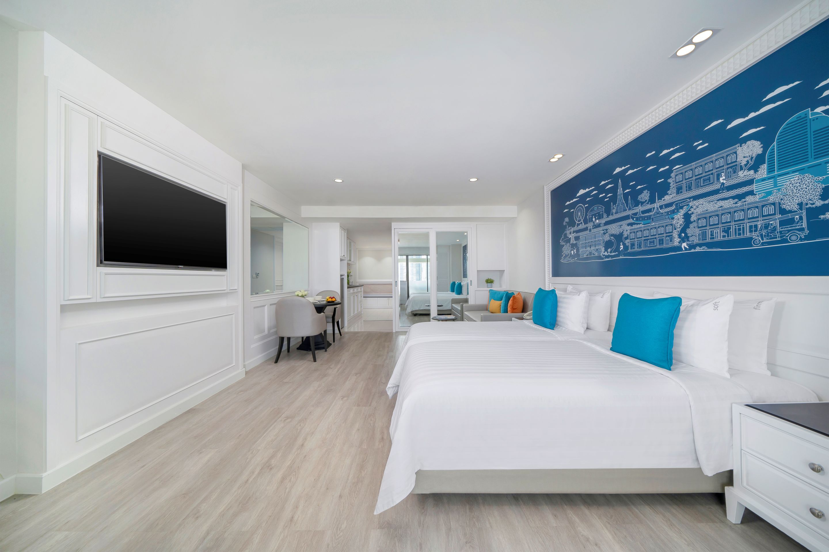 A modern hotel room with a large bed, a flat-screen TV, a dining area, and a bathroom.