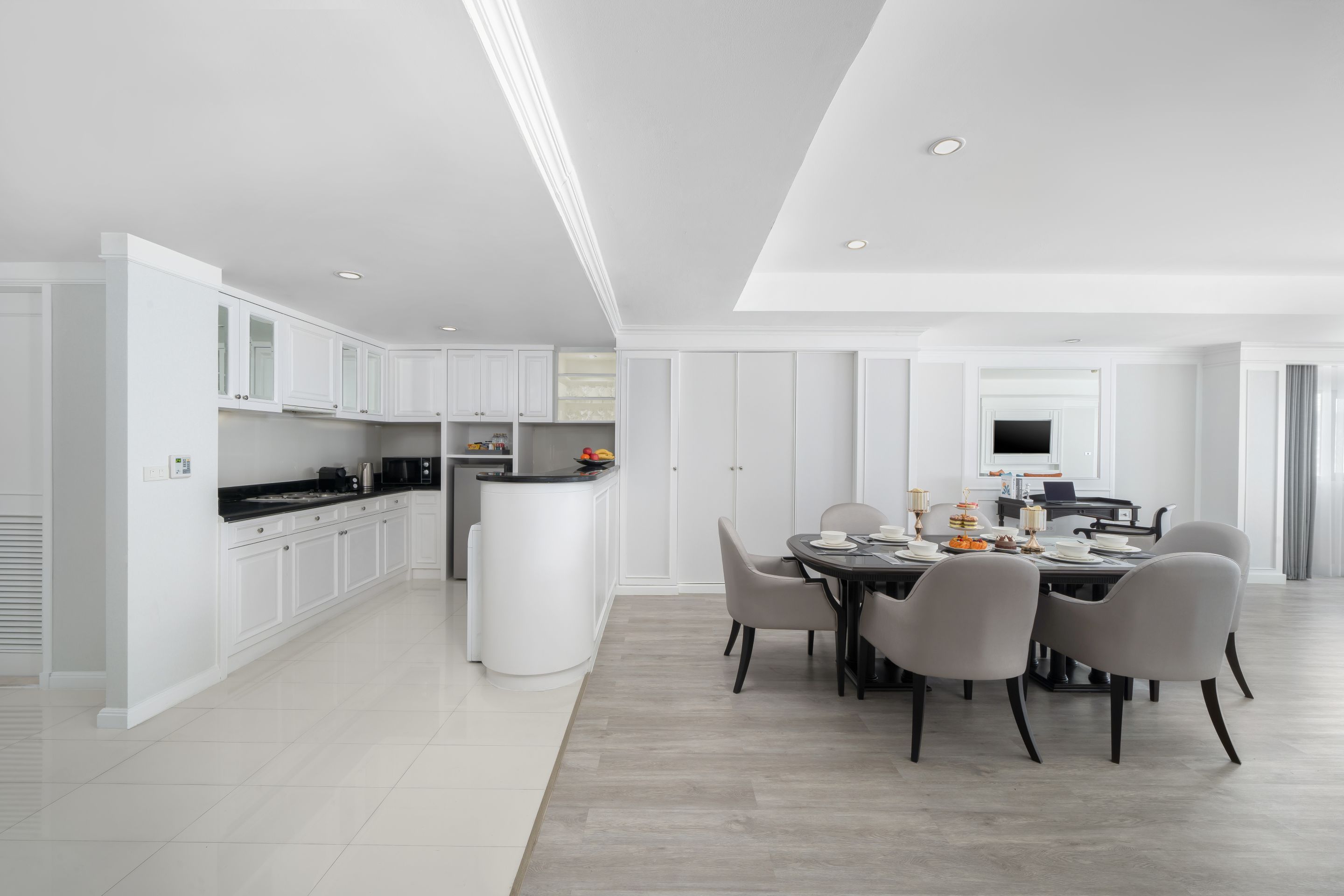 Une cuisine moderne avec des meubles blancs, un îlot central et un coin repas avec une table dressée pour six personnes.