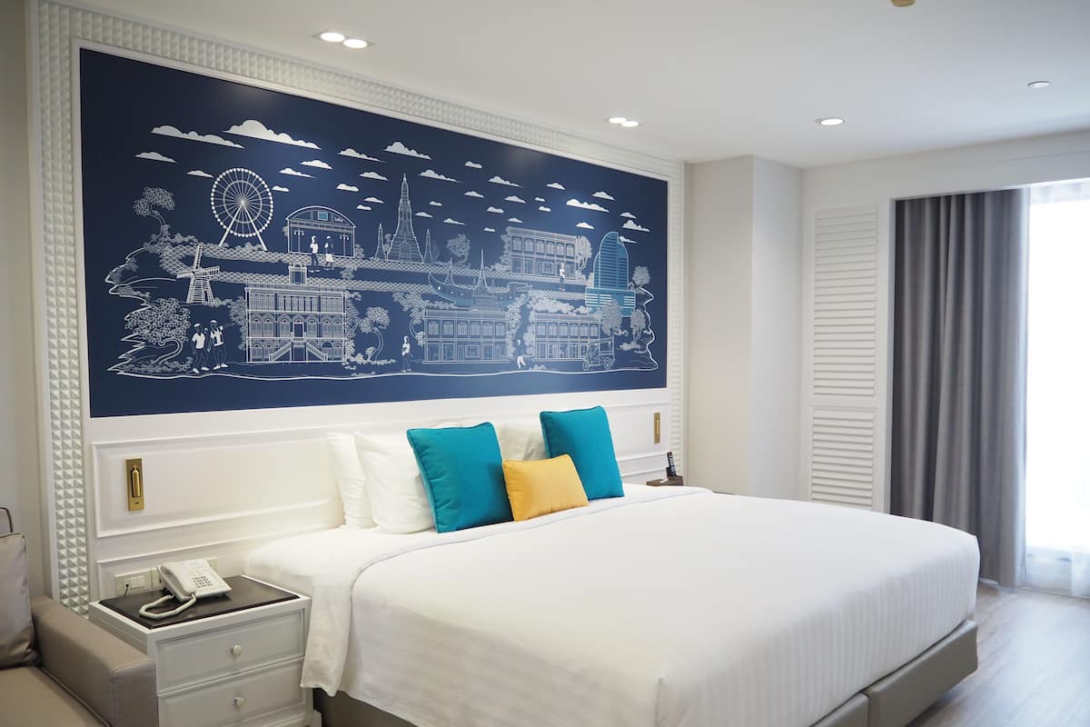 Een hotelkamer met een groot bed, een nachtkastje met een telefoon en een muurschildering van een stadsgezicht.