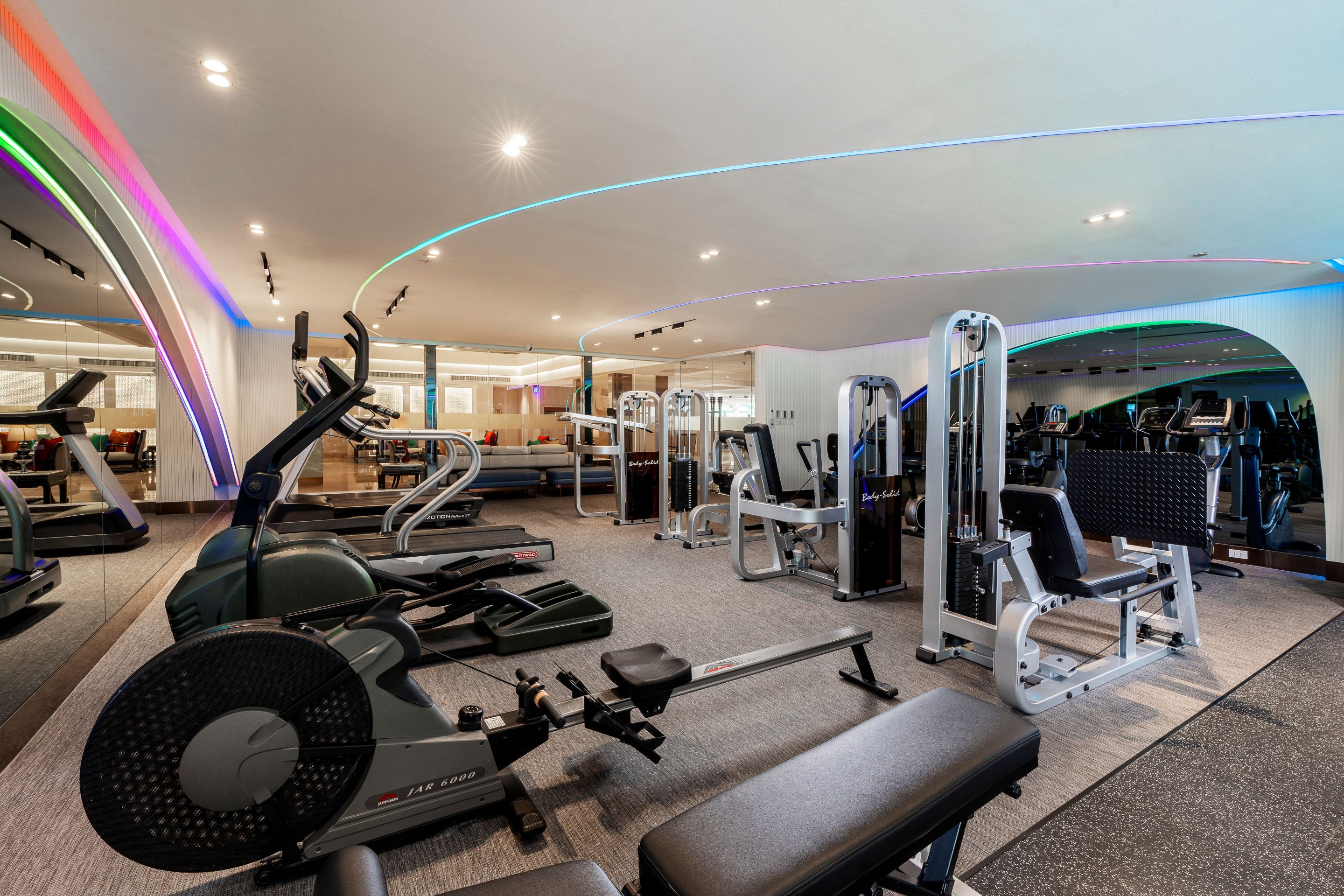 Un gimnasio con diversos equipos de ejercicio, incluyendo cintas de correr, máquinas de pesas y un banco.