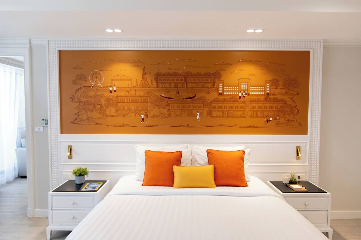 Een hotelkamer met een groot bed, witte nachtkastjes en een muurschildering met daarop een stadsgezicht.