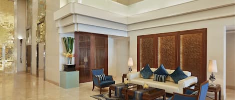 A spacious lobby with a high ceiling, a central seating area with a sofa and chairs, a reception desk, and a decorative wall with vertical panels.