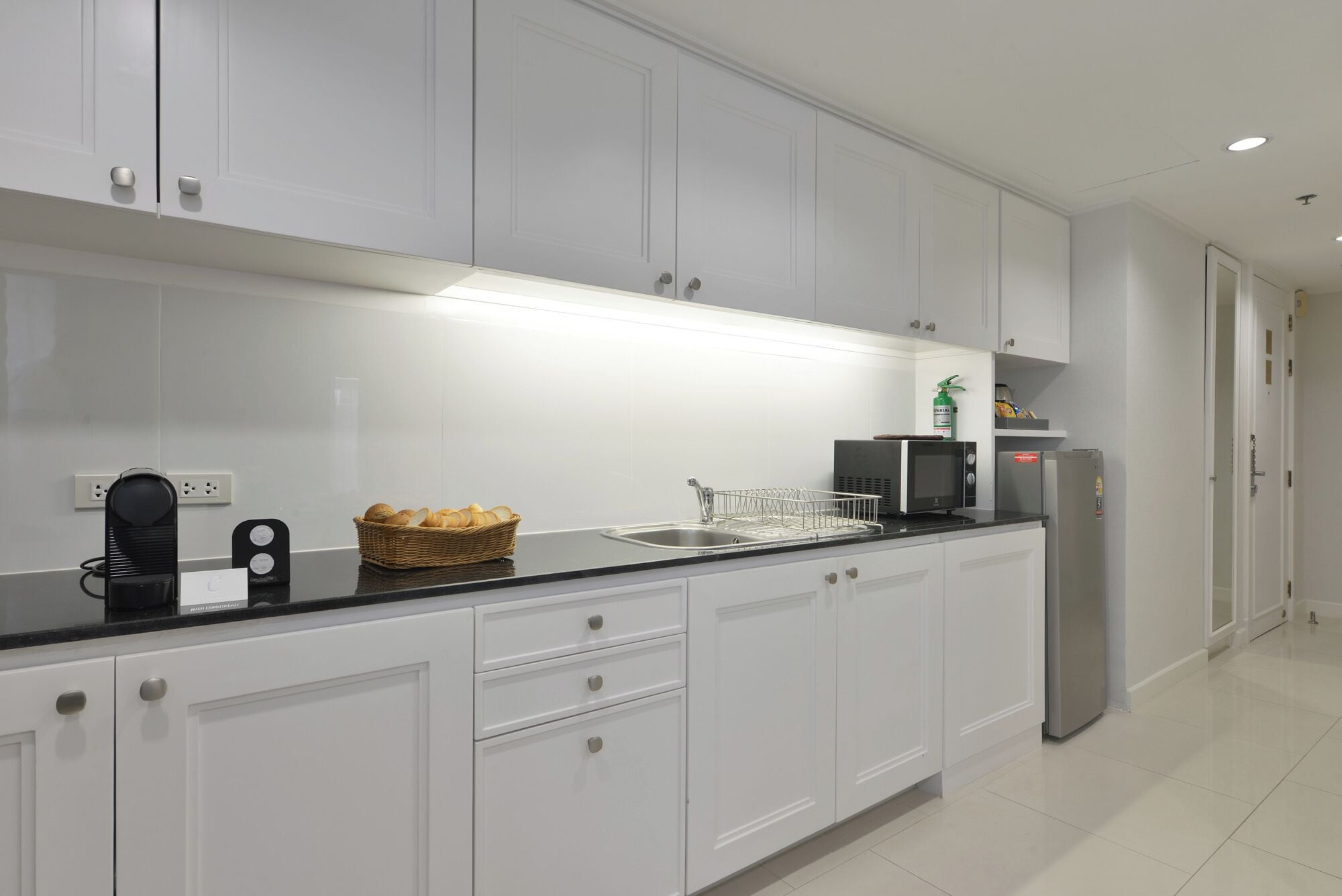 Een moderne keuken met witte kasten, een zwart aanrecht, een roestvrijstalen spoelbak, een magnetron en een koelkast.