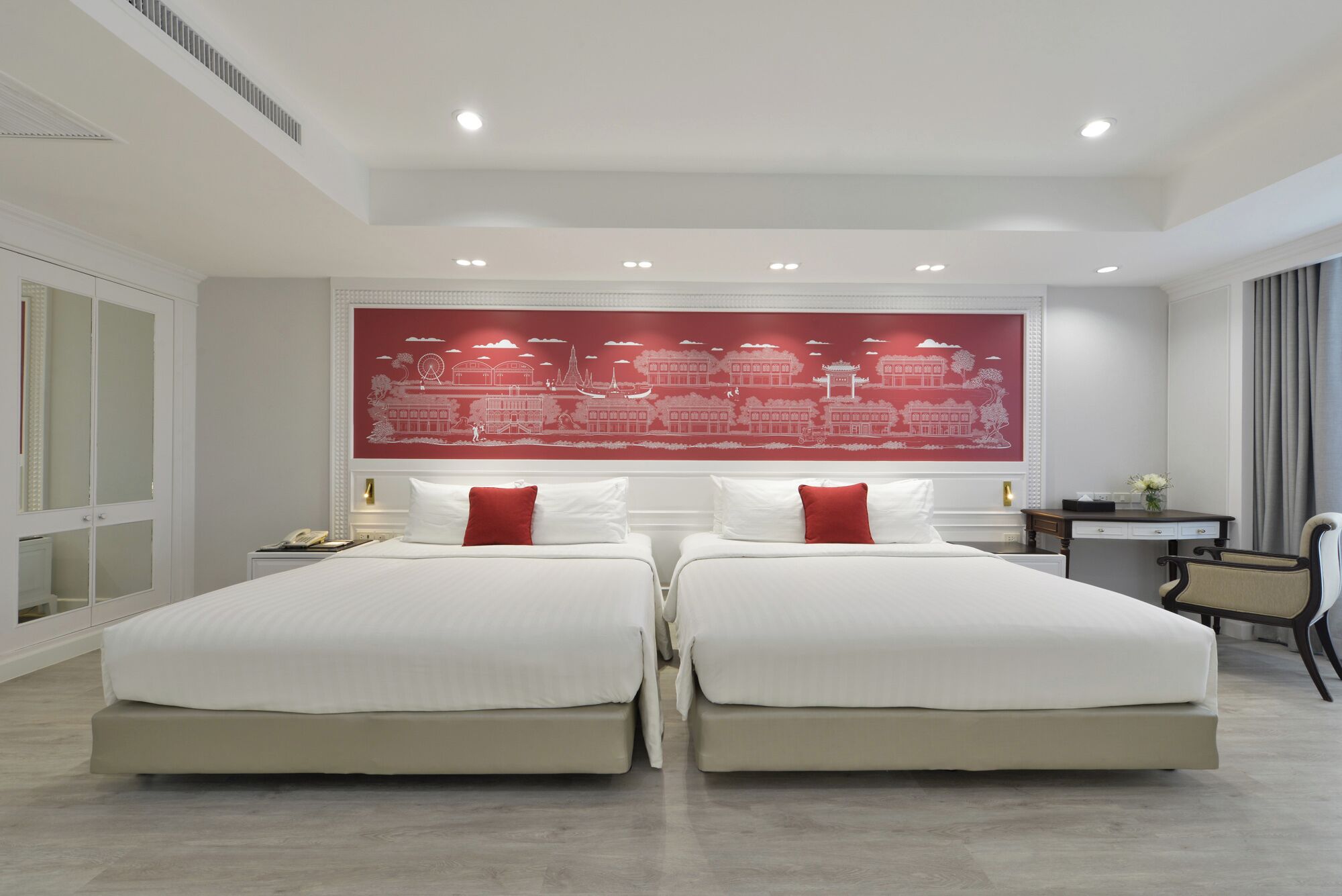 A hotel room with two beds, a large red cityscape mural on the wall, a desk, and a chair.