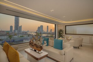 A modern living room with a large window, a model ship, and a city view. - Centre Point Plus Hotel Silom (Bangkok)