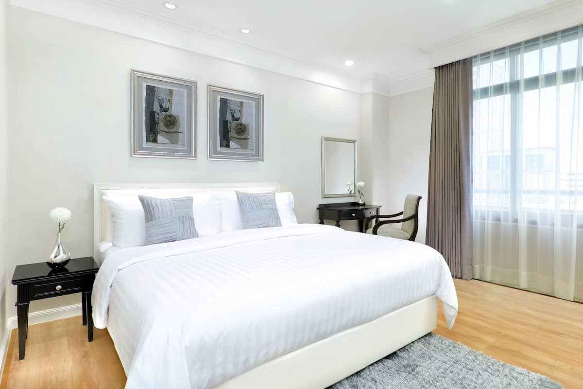 A modern hotel room with a large bed, a desk, and a chair. There are two framed pictures on the wall and a window with curtains.