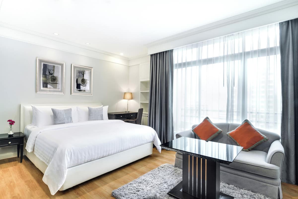 A modern hotel room with a large bed, a sofa, a desk, and a window with curtains.