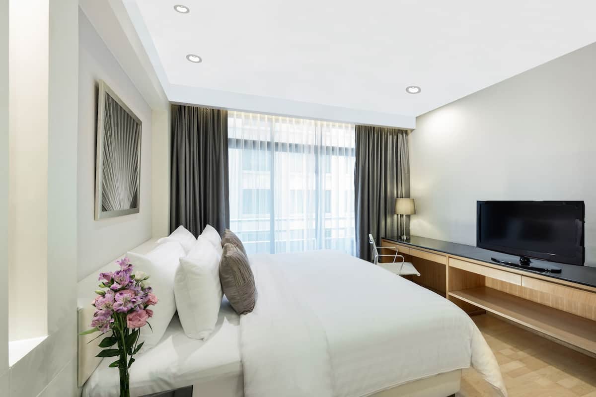 A modern hotel room with a large bed, a flat-screen TV, a desk, and a large window with curtains.