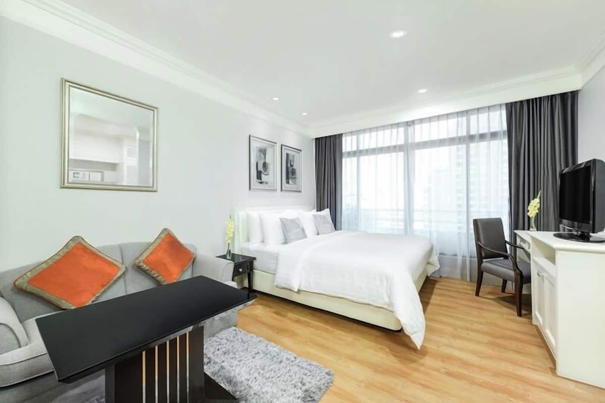 A hotel room with a bed, a desk, a chair, a TV, and a window with curtains.