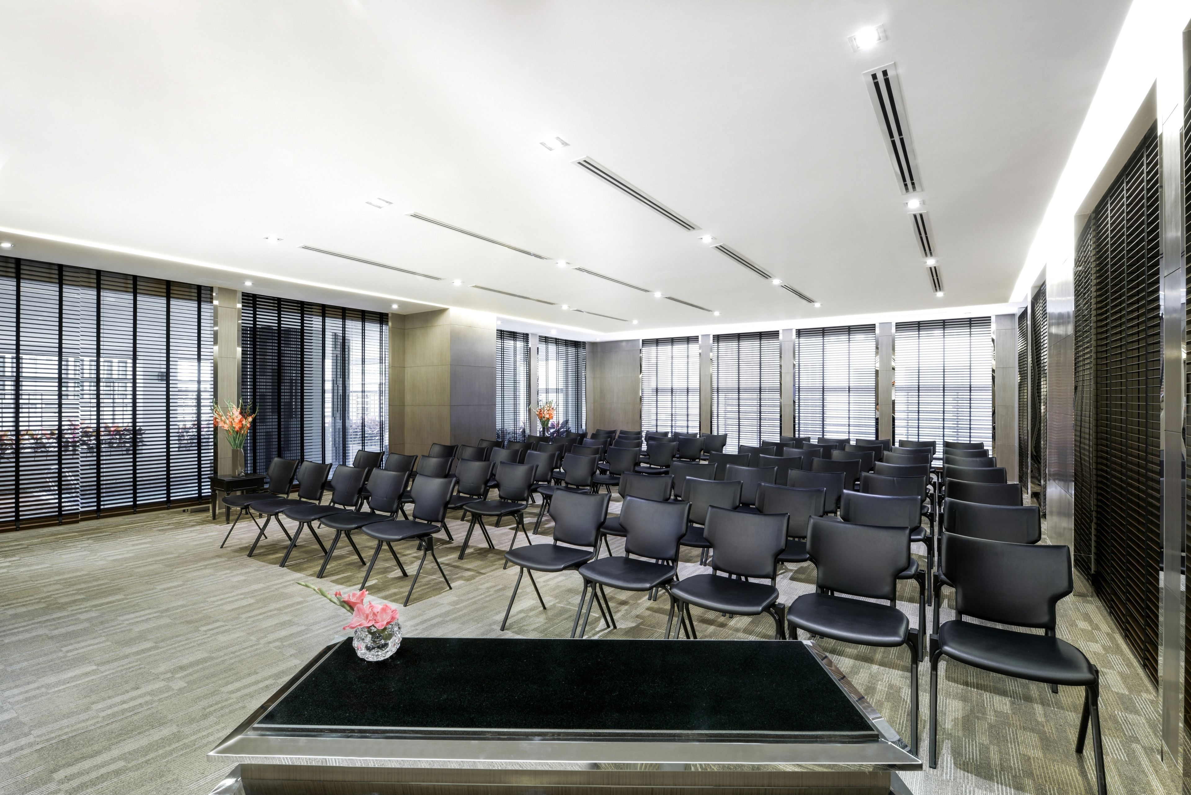 Un salón de conferencias con filas de sillas, una mesa negra y un jarrón con flores.