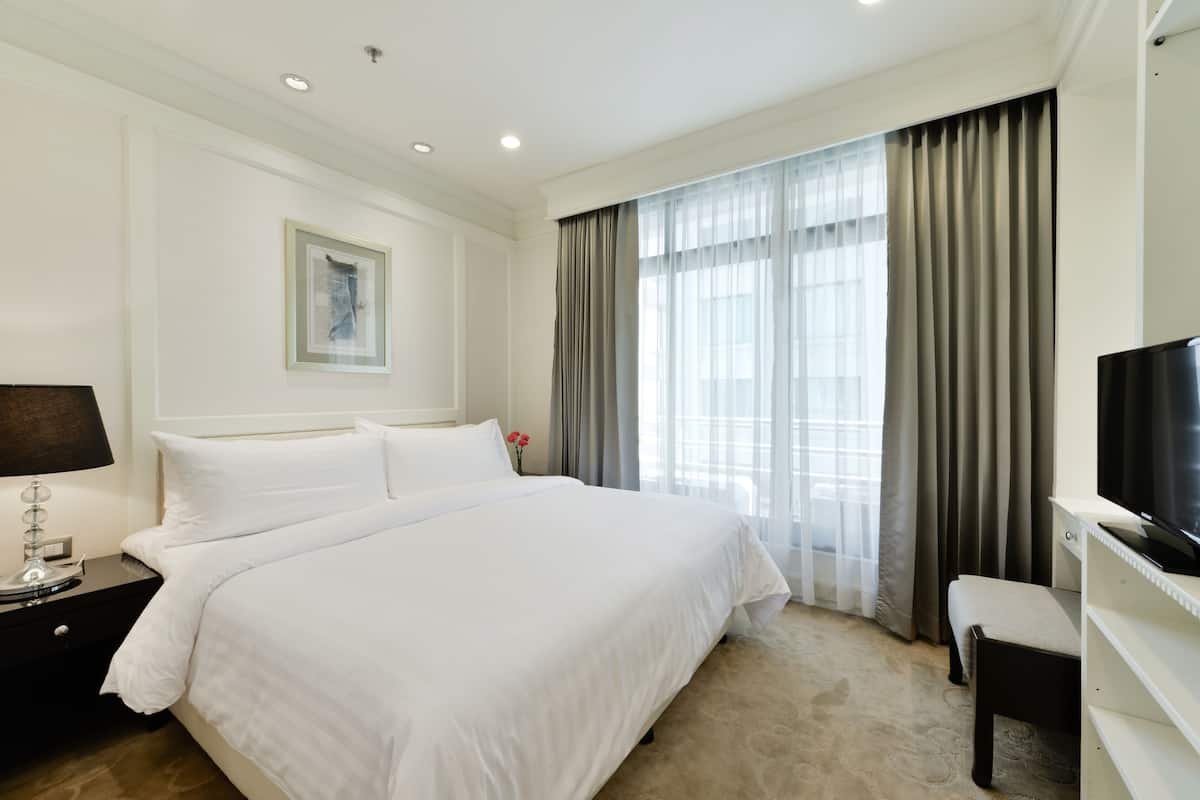 A hotel room with a large bed, a bedside table with a lamp, a TV, and a window with curtains.