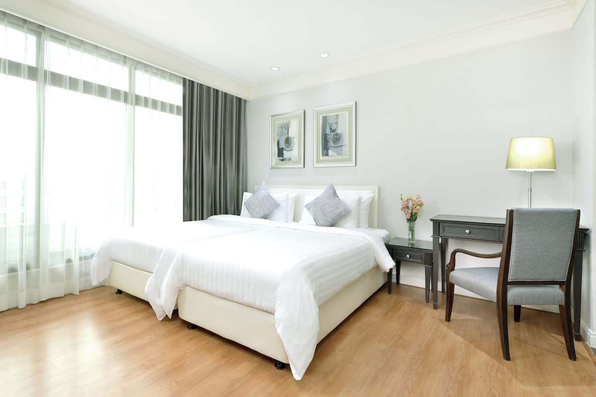 A hotel room with a large bed, a desk, and a chair. There are two framed pictures on the wall, a lamp on the desk, and a window with curtains.