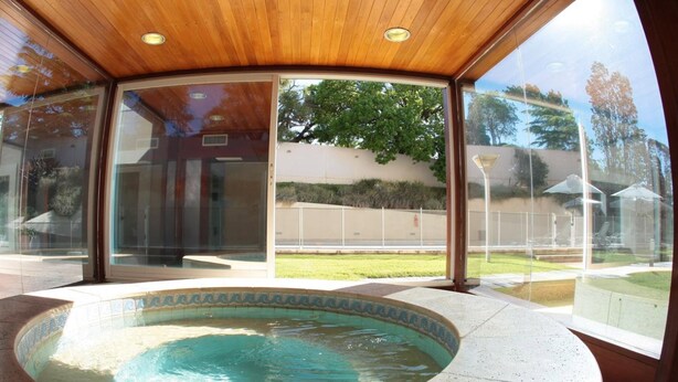 A modern indoor swimming pool with a wooden ceiling and glass walls offering views of a residential area.