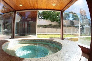 Piscina interior moderna con techo de madera y paredes de vidrio que ofrecen vistas a una zona residencial.