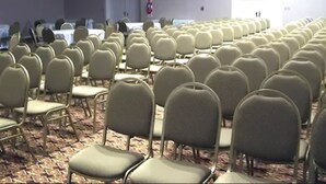 A conference room with rows of chairs and tables, carpeted floor, and a fire extinguisher on the wall.