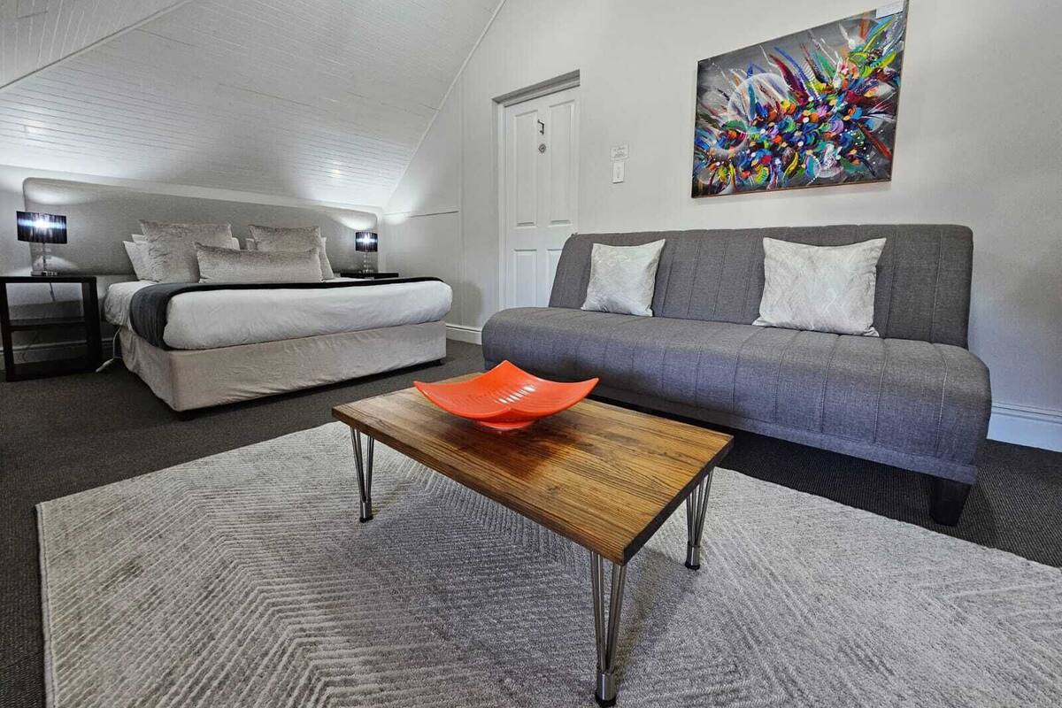 A modern bedroom with a bed, a gray sofa, and a colorful abstract painting on the wall.