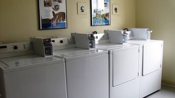 Een wasserette met vier witte wasmachines en drogers, een poster op de muur met daarop Motel 6, en een lichtschakelaar.