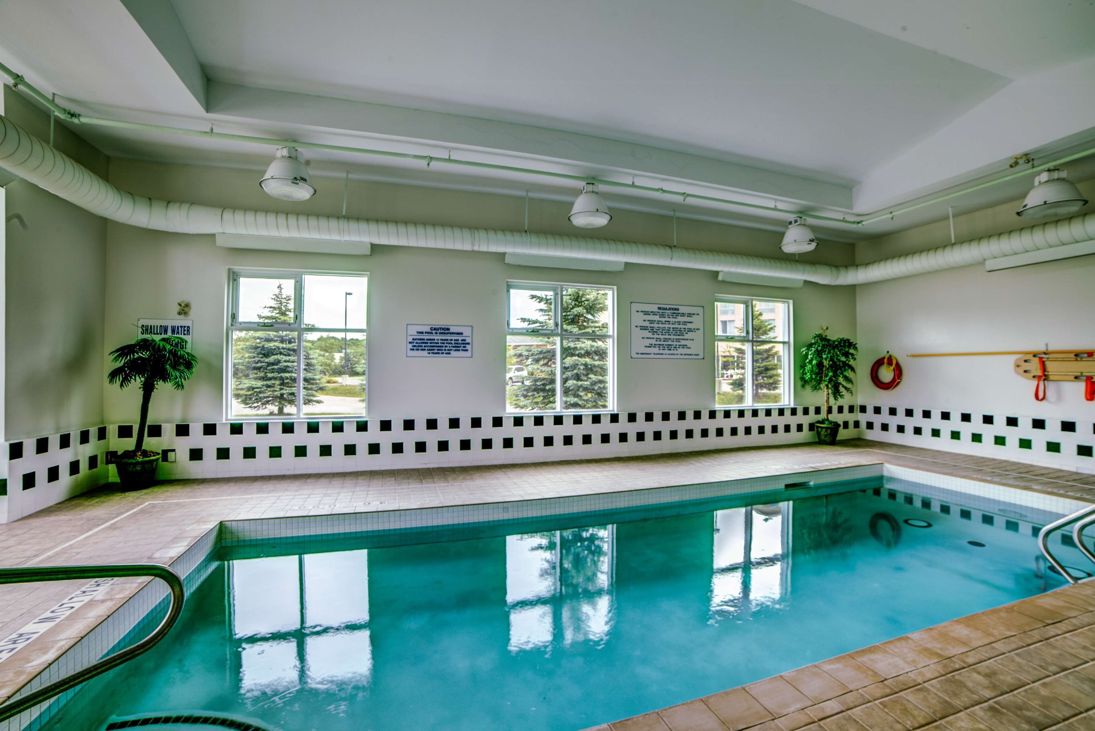 An indoor swimming pool with clear windows, safety signs, and a lifebuoy on the wall.
