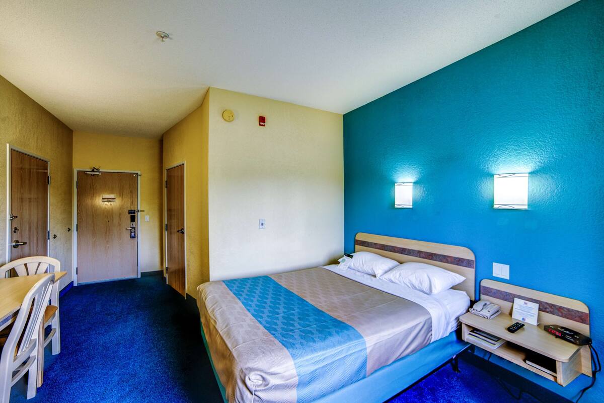 Hotellihuone, jossa on sänky, yöpöytä, tuoli ja työpöytä, jossa on myös tuoli.