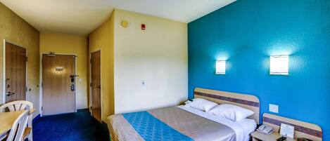 A hotel room with a bed, bedside table, chair, and a desk with a chair.