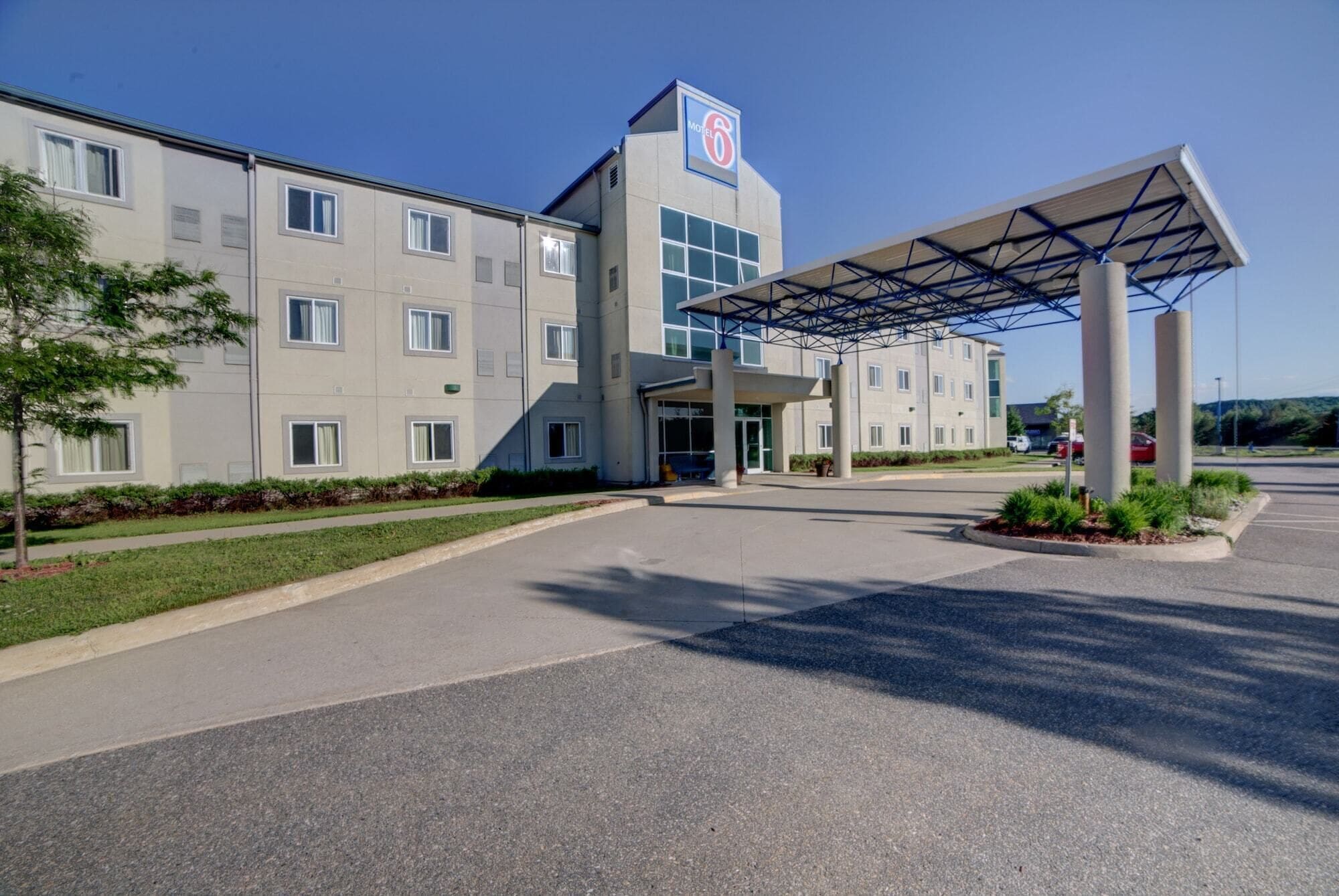 A modern hotel with a prominent '6' sign, a covered entrance, and a parking area.