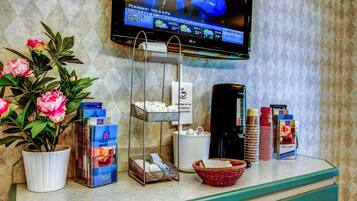 A hotel reception area with a TV displaying weather information, a potted plant, magazines, and various amenities like a coffee maker and a basket.