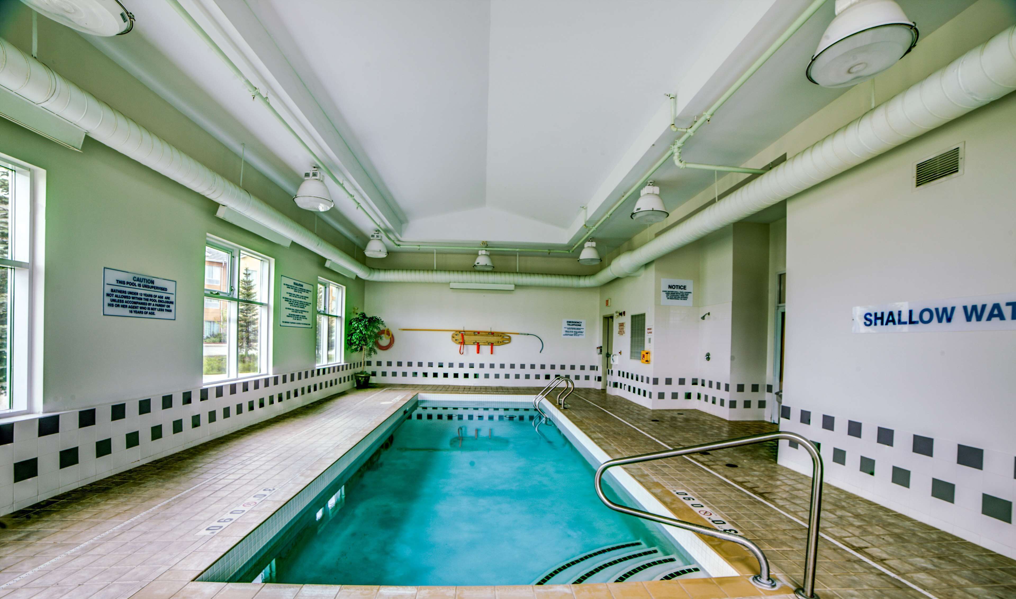 An indoor swimming pool with clear signage, including a caution sign and a shallow water warning.